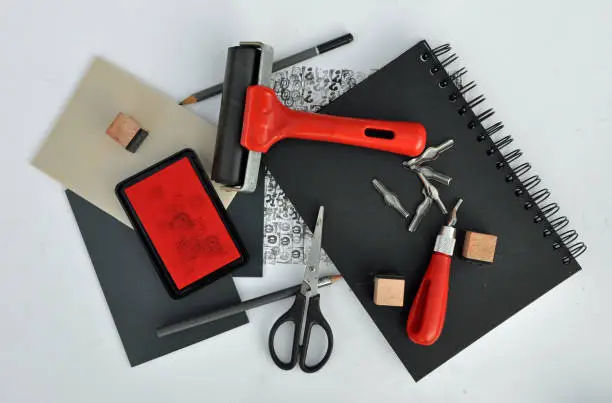 Studio set up flat lay. Creative art and craft hobby or leisure activity materials. Coronavirus lockdown pastime. Lino cutting and relief or block printing. Including, ink pad, blocks, sketchbook, roller, brayer, cutting tools and sheets of lino.