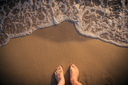 Feet with wave on sandy beach top