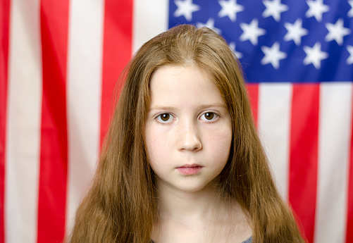 Sad red-haired girl looks at the camera. Girl on the background of the flag of America