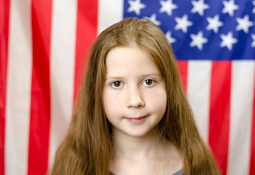 The red-haired girl looks at the camera and smiles. Girl on the background of the flag of America