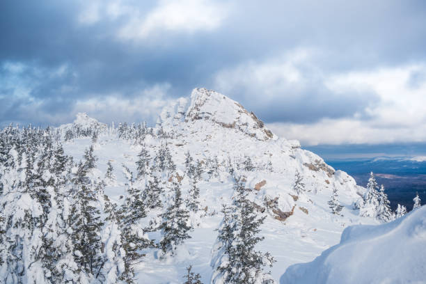 istock Winter landscape with snow forest on hillside, rocks under cloudy sky 1296867885