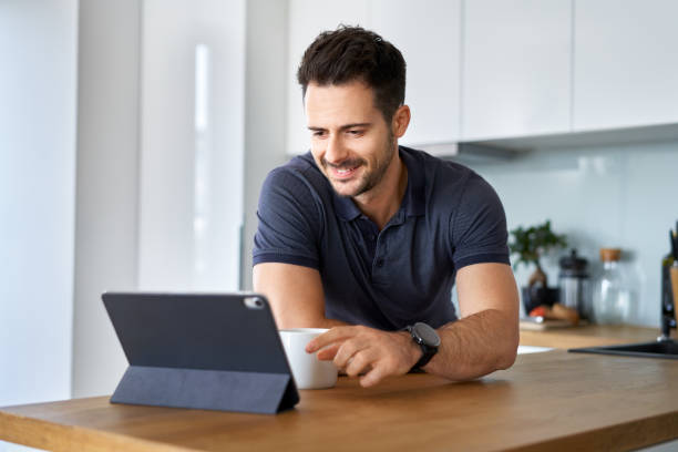 istock Happy man having morning coffee using digital tablet at home 1296870722