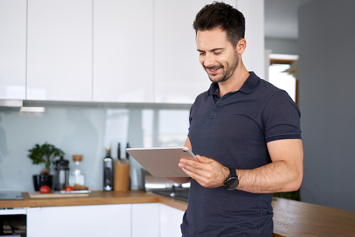 Man standing in kitchen using digital tablet