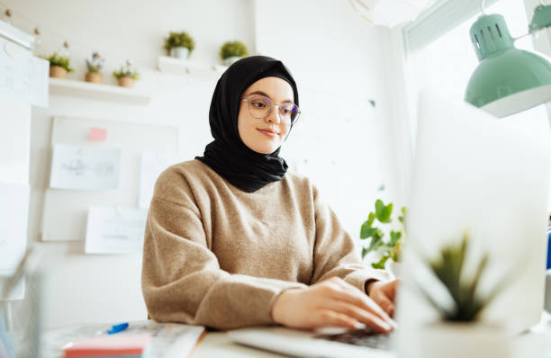 istock Middle Eastern female software engineer with hijab and glasses working on laptop in office 1296872751