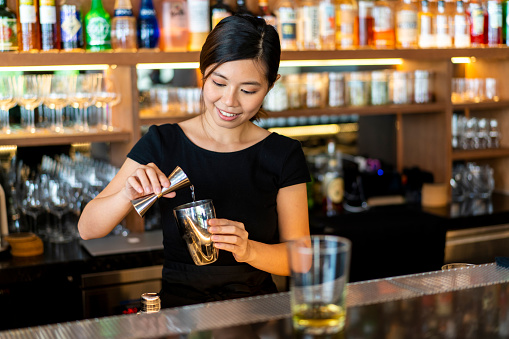 Asian female Bartender mixing a drink at a local bar.