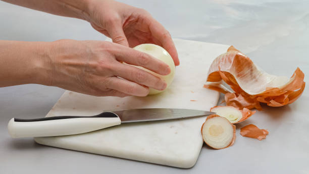 istock Peeling white onion on marble cutting board. Close up cooking process, woman hands, marble kitchen table background 1296876590