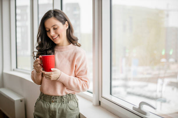 istock Young woman drinking coffee and day dreaming while looking through window 1296876838