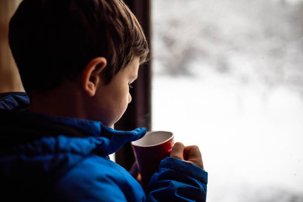 istock A boy drinking hot tea in front of the window 1296878525