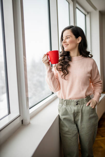 istock Young woman drinking coffee and day dreaming while looking through window 1296879989
