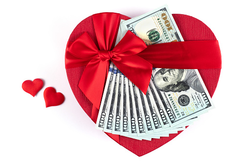 Gift box in the form of a human heart symbol with 100 USD bills on a white background