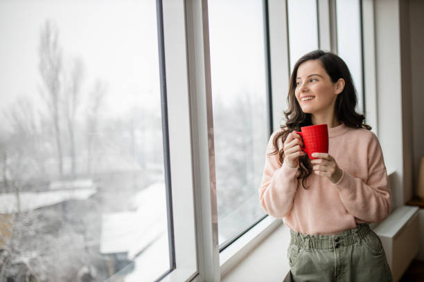 istock Young woman drinking coffee and day dreaming while looking through window 1296880118