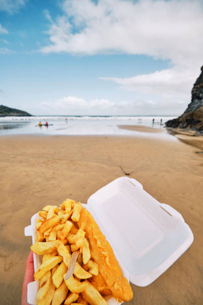 Wide angle POV view of a Carton of Fish and Chips at Towan Beach, Newquay, Cornwall on a sunny Autumn day.