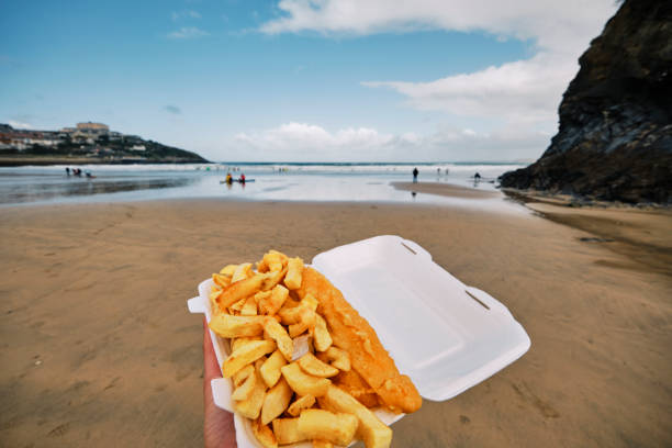 Wide angle POV view of a Carton of Fish and Chips at Towan Beach, Newquay, Cornwall on a sunny Autumn day.