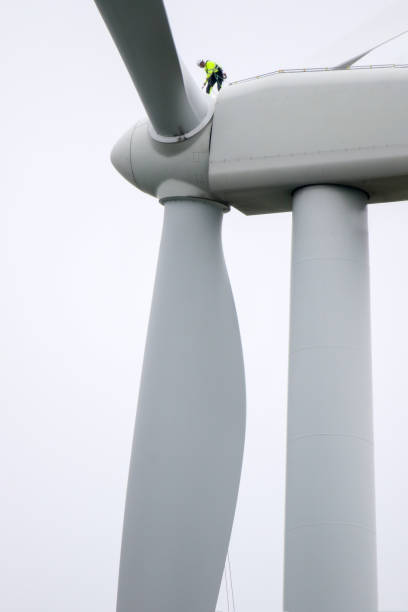 istock Epic view on Professional rope access technician standing on roof (hub) of wind turbine and pulling rope up. 1296881550