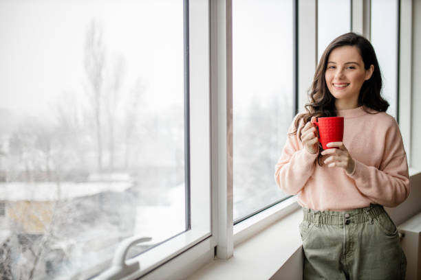 istock Young woman drinking coffee and day dreaming while looking through window 1296883560