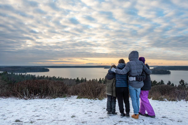 Family together holding each other and looking at a view. Mountain top winter sunset snow scene with water and horizon. stock photo