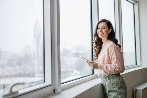 istock Beautiful young woman using her digital tablet and standing by window at home 1296886594