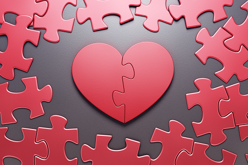 Jigsaw puzzle in form of a heart symbol composed from two halves, which are in center amongst the ordinary pieces of another jigsaw puzzle. 3D rendering graphics on the theme of Valentine's Day.