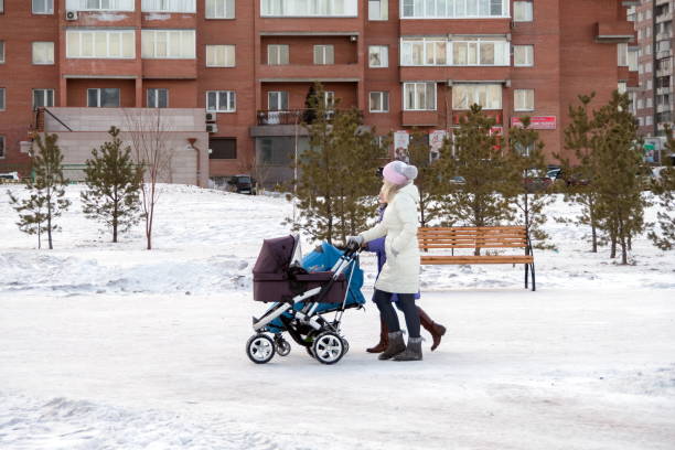 Two young mothers are walking with strollers along a winter snow-covered street against the backdrop of residential buildings. Krasnoyarsk, Krasnoyarsk Region, RF - January 8, 2017: Two young mothers are walking with strollers along a winter snow-covered street against the backdrop of residential buildings. krasnoyarsk photos stock pictures, royalty-free photos & images