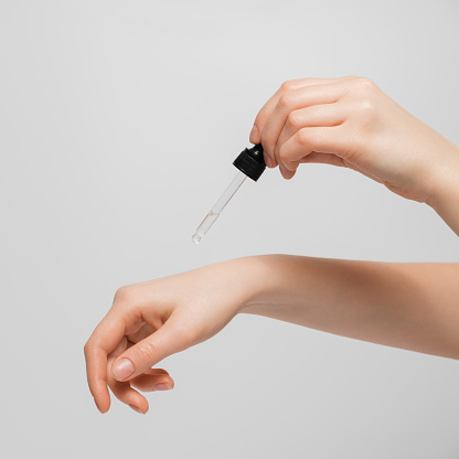 Hand of woman with pipette drop of serum or hyaluronic acid on gray background. Hands of a beautiful woman dripping serum collagen.