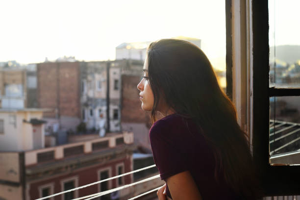 Girl profile in the window at sunset Profile portrait of a beautiful young woman at the window looking towards the street in serene attitude looking through window stock pictures, royalty-free photos & images