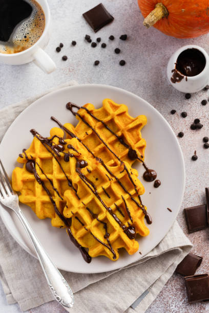 Pumpkin waffles with chocolate and icing sugar served for breakfast on light background and old rustic breakfast table. Selective focus.
