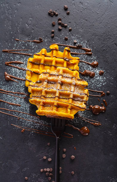 Pumpkin waffles with chocolate and sugar powder strung on forkon dark old background. Top view