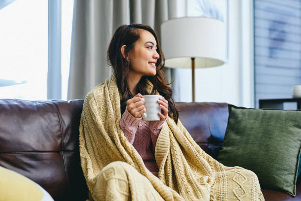 Coffee is what puts me in a good mood Shot of a woman sitting at home with a hot beverage and a blanket blanket stock pictures, royalty-free photos & images