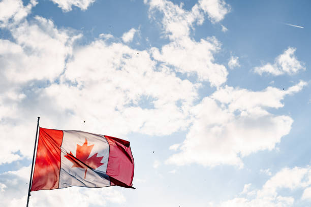 istock Flag of Canada with red and white vertical stripes and a maple leaf against the sky and clouds. 1296895113