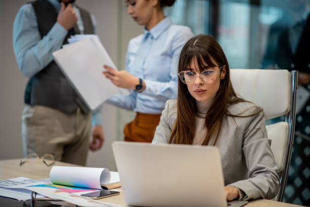 istock Young business woman with eyeglasses using laptop for paperwork. 1296899304