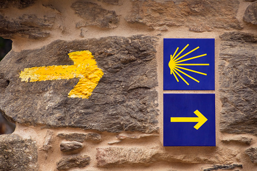 Camino de Santiago, old pilgrimage footpath, pilgrim signs  and symbols on stone wall, scallop and yellow arrow symbol.  Unesco World Heritage site. Año Santo, Camino francés, Lugo province, Galicia, Spain.
