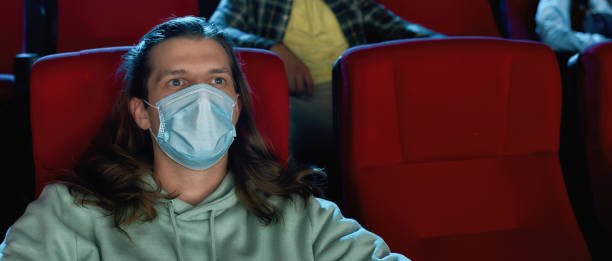 istock Young guy wearing protective face masks while watching movie in cinema auditorium during covid19 pandemic 1296903006