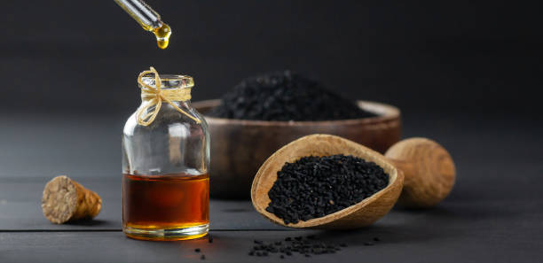 bottiglia di vetro di olio essenziale di semi di cumino nero, nigella sativa in scoop su sfondo di legno nero, olio gocciolante - caraway foto e immagini stock