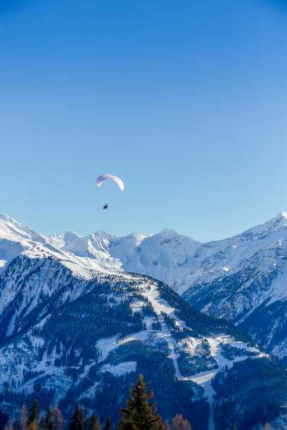 Spring time reveals the texture of the trees on the mountains below - the highest peaks still covered in snow, a pair of paragliders float tranquilly above