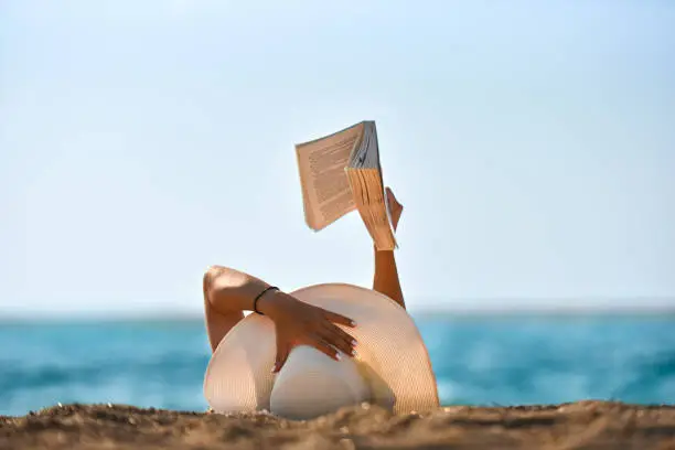 Photo of Young woman reads a book on the beach stock photo