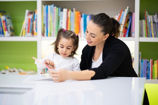 In the library of the kids club, the little girl and her teacher examine picture books