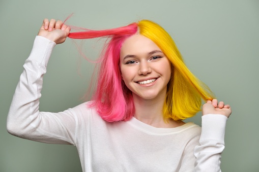 Dyed long hair close-up, girl fashion beauty model showing coloring on her hair, green studio background. Professional coloring, beauty, fashion, trends