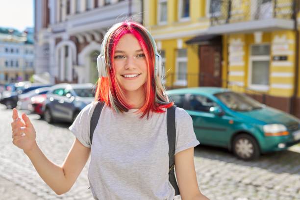 Outdoor portrait of teenage girl listening music with wireless headphones Outdoor portrait of beautiful trending teenage girl listening music with wireless headphones. Happy smiling female with trendy colored hairstyle on street of sunny summer city pink hair stock pictures, royalty-free photos & images