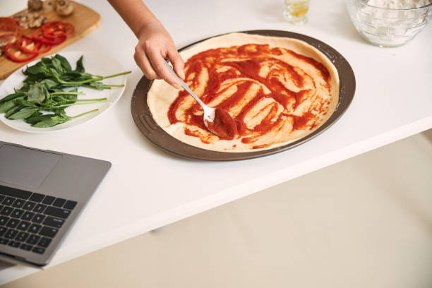 istock Covering the flat dough surface with tomato sauce 1296921663