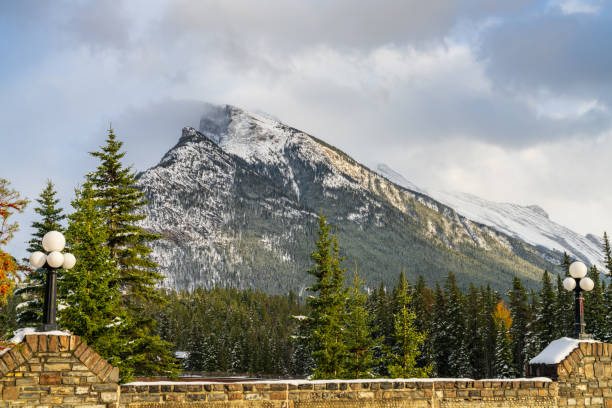 Snow-covered Mount Rundle mountain range with snowy forest over blue sky and white clouds in winter sunny day. Banff National Park, Canadian Rockies.