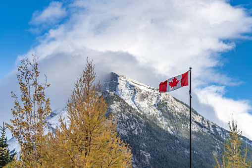 National Flag of Canada with Mount Rundle mountain range in a snowy sunny day. Banff National Park, Canadian Rockies.