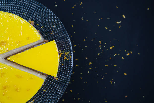 istock Sliced ​​lemon cheesecake on glass plate at black background. 1296926804