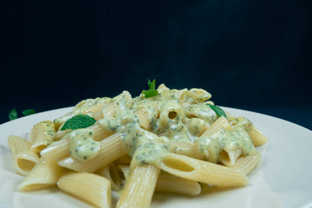 Penne pasta with pesto sauce and basil on a plate, isolated on white background
