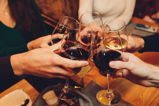 Close up shot of group of people clinking glasses with wine or champagne in front of bokeh background. older people hands