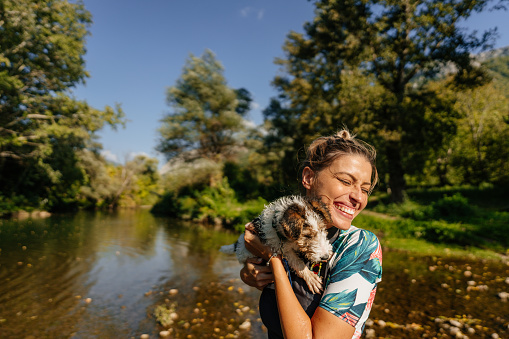 Photo of a smiling young woman and her cute puppy enjoying the hot, sunny day by the river.