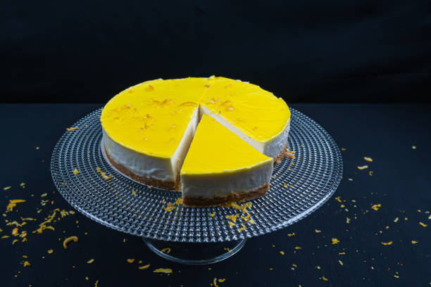 istock Sliced ​​lemon cheesecake on glass plate at black background. (Copyspace) 1296933973