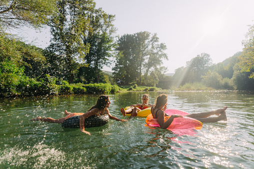 Photo of teenage girls swimming in the river while hanging out in nature; enjoying their youth and friendship and spending a hot summer day outdoors.