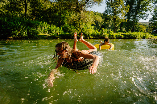 Photo of a teenage girl swimming in the river while hanging out in nature with her friend; enjoying their youth and friendship and spending a hot summer day outdoors.