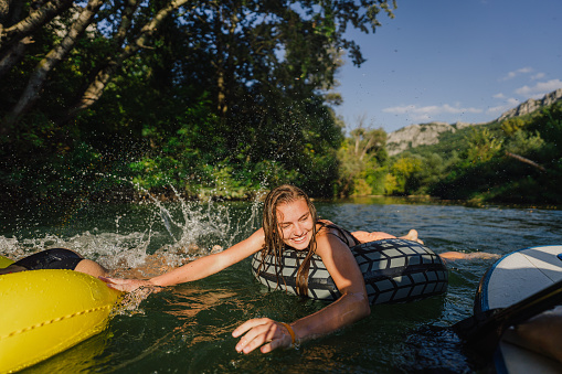 Photo of a teenage girl swimming and paddling on the river while hanging out in nature with her friends; enjoying their youth and friendship and spending a hot summer day outdoors.