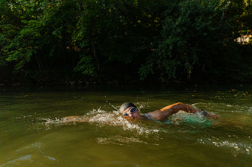 Photo of a teenage girl swimming in the river; she is wearing swimming goggles and a swimming cap.